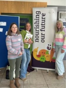 Three women standing beside a Nourishing Our Future banner at a training event