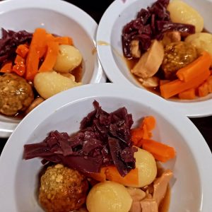 Three bowls of dinner with potatoes, carrots, red cabbage, a stuffing ball and sliced meat in gravy